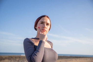Plajda düşünceli bir yüz ifadesi olan genç bir kadın, sağ tarafta fotokopi odası var..