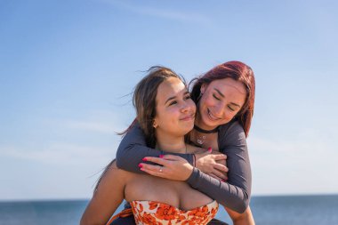 İki kız kardeş deniz kenarında birlikte eğleniyor, biri diğerini sırtında kaldırıyor..