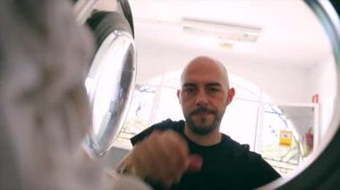 Bir adam çamaşır makinesini kirli çamaşırlarla, çamaşır makinesiyle doldurur.