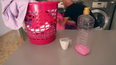 Bir adam çamaşır odasında çamaşır makinesini çarşafla dolduruyor, kirli çamaşır sepetine yakın çekim yapıyor.