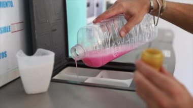 Çamaşırhanede çamaşır yıkamak için çamaşır makinesine deterjan döken bir adam.