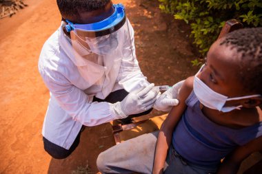 Bir doktor, tıbbi bir ziyaret sırasında Afrika 'da bir çocuğa aşı yapar.