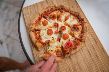 Dilimlenmiş bir pizza, bir çocuk onu yemek için bir dilim alıyor.