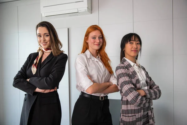 Three happy businesswomen with folded arms and confident expressions pose in the office