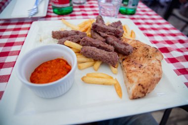 Cevapcici, tipik Balkan mutfağı olan kızarmış patates, ekmek ve kırmızı sosla servis ediliyor