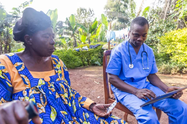 Bir doktor tabletindeki reçeteye danışır ve Afrika 'daki yaşlı hastasına uyuşturucu verir.