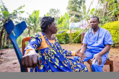 Yaşlı, hasta bir Afrikalı kadın ev ziyaretinde doktora belirtilerini anlatıyor..