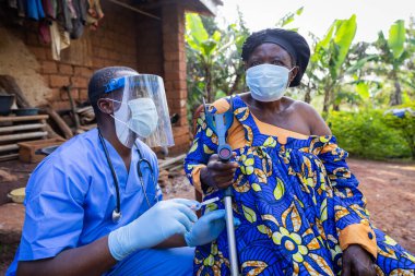 Genç Afrikalı doktor yaşlı bir kadına bir doz aşı enjekte etmeye hazırlanıyor..