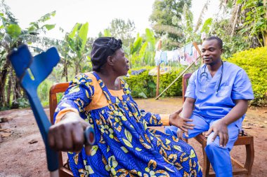 Yaşlı, hasta bir Afrikalı kadın ev ziyaretinde doktora belirtilerini anlatıyor..