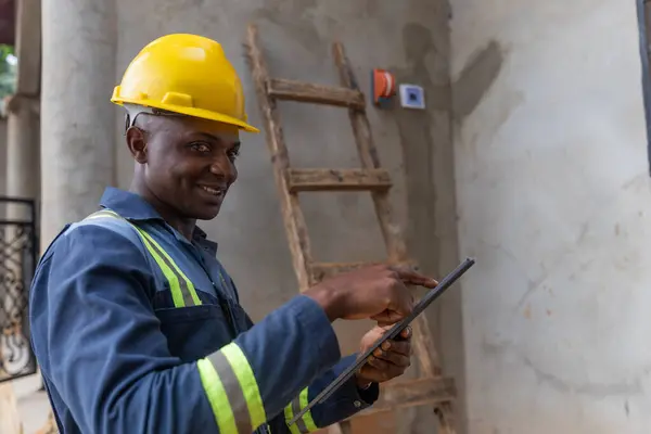 Smiling African electrician holds up his tablet at work. Electricity concept.