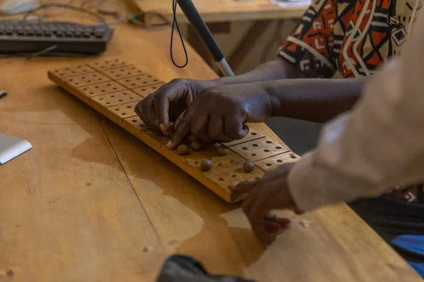 Blind African person learning to use the braille number tablet under the guidance of a teacher.