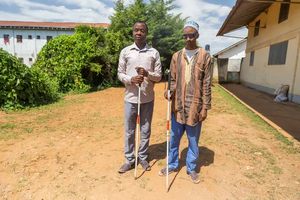 Blind friends stand still then continue for a walk while helping themselves with their white canes.