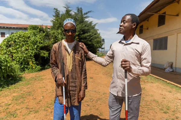 Blind man walking with his friend who is also blind touches his shoulder.