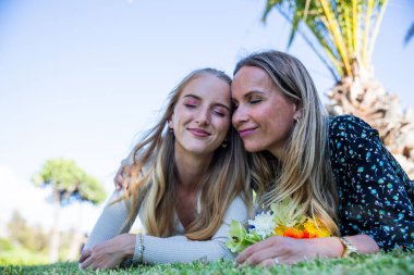 Anne ve kızı gözleri kapalı çimlerin üzerinde uzanıyorlar, birlik ve aşk kavramı.