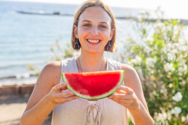 Bir kadın elinde karpuz dilimiyle kameraya gülümsüyor..