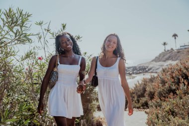 İki kadın el ele tutuşarak bir yolda yürüyor, yazın en iyi arkadaşlar birlikte..