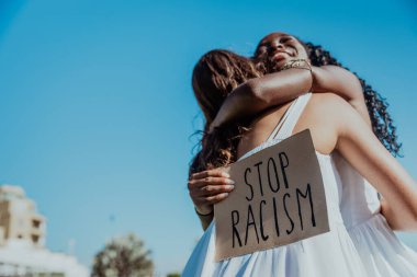 Two happy women hug each other during a protest against racism. clipart