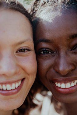 İki kadın kameraya gülümsüyor, biri daha koyu tenli. Sahne mutlu ve dostane.