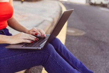 Önünde dizüstü bilgisayar açık bir şekilde yerde oturan bir kadın. Klavyeye yazı yazıyor ve işine odaklanmış durumda. Verimlilik ve konsantrasyon kavramı