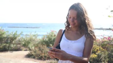 Bir kız, yaz tatilinde tropik bir yerde telefonunu kullanıyor.