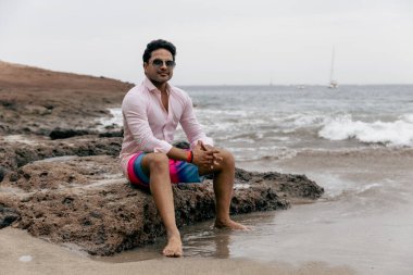 Başarılı bir Hintli adam sahilde dinlenirken bir kayanın üzerinde oturur.