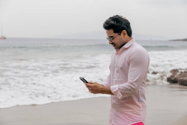 Kumsalda bir adam telefonuyla yazı yazıyor. Bulutlu bir gün.