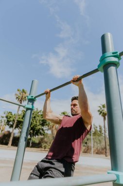 Bir adam açık hava spor salonunda yüksek çıtayla antrenman yapıyor, açık gökyüzü ve tropik konum.