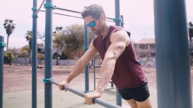 Orta yaşlı, formda bir adam açık hava jimnastik salonunda barın üstünde şınav çekiyor.