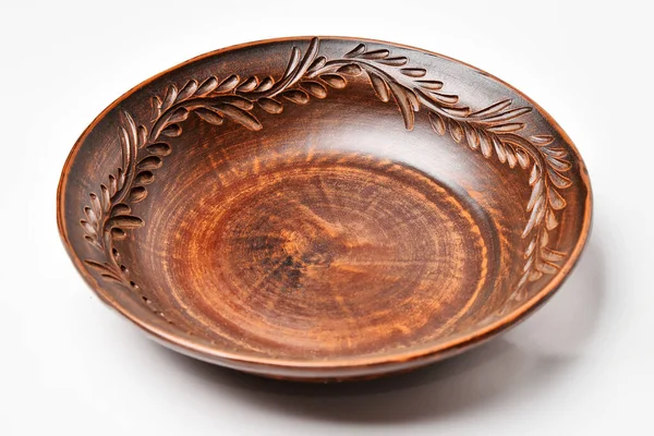 Ceramic plate, earthenware. Pottery plate with a pattern of branch with leaves on the edge, on a white background. Brown ceramic tableware, rustic style, kitchen utensils