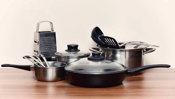 Metal kitchen utensils for cooking on a wooden table. Pot, frying pan, container, grater, spatulas.