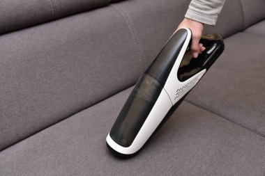 Elektrikli süpürgeyle Kadın Temizleme Kanepesi, yakın görüş. Ev hanımı kanepeyi temizliyor. Kablosuz taşınabilir elektrikli süpürge..