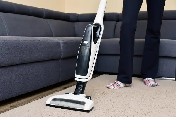 Woman cleaning the living room with wireless vacuum cleaner. Housewife chores. Work at home vacuum the carpet near the sofa. Cleaning and collecting hair from domestic animals - cats, dogs.