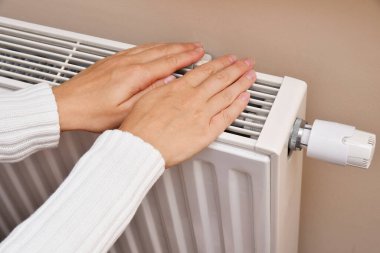 Bir kadın ellerini kaloriferin yanında ısıtır.