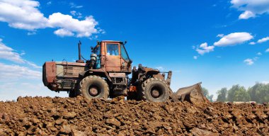 İnşaat alanında büyük, ağır bir buldozer. Arka planda açık mavi gökyüzü olan bir toprak yığını üzerine kurulmuş..