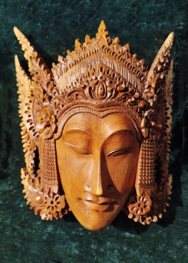 Huzurlu bir yüz ve ayrıntılı bir başlık, Bali sanatı veya Güneydoğu Asya sanatı tasvir eden karmaşık bir ahşap maske..