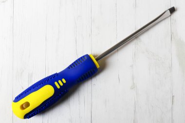 Tahta arka planda sarı-mavi saplı düz bir tornavida.