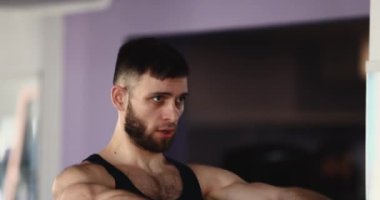 Spor salonunda dambıllarla omuz egzersizi yapan bir adam.