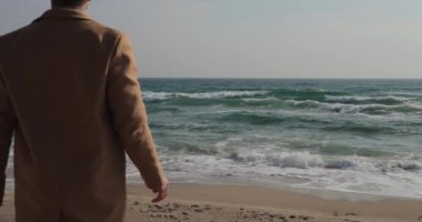 Kıyı şeridinde duran paltolu bir adam, 120 fps 'de yavaş çekimde 4k.