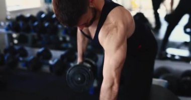 Spor salonunda tek kollu dambıl sırasına giren bir adam.