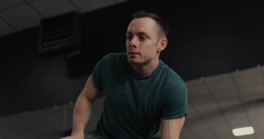 Güçlü bir adam spor salonunda halteri kaldırıyor ve kaslarını şişiriyor.