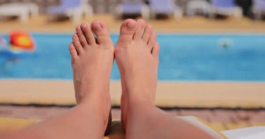 Tatil günü mavi su havuzunun yanında uzanan çıplak ayaklı kadın bacakları dinleniyor.