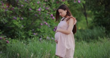 Hamile bir kadın karnına dokunuyor. Doğada duruyor. Yavaş çekim.