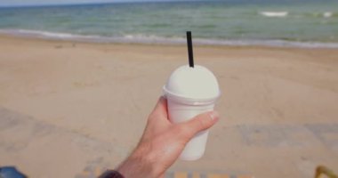 Pov erkeği elinde milkshake, deniz kenarında kokteyl içiyor.
