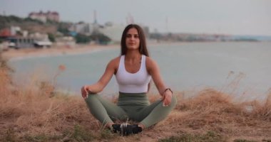 Yoga egzersizi yapan sporcu kadın denizin karşısındaki bir tepede poz veriyor.