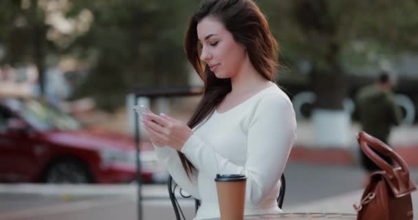 アウトドアカフェで座っているスマートフォンを使った女性 スローモーション — ストック動画