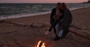 Akşamları kumsalda, ateşin yanında şefkatle oturan çift.