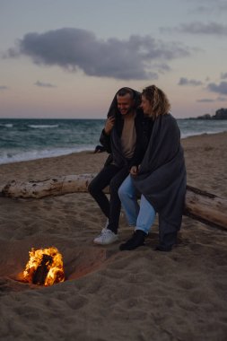 Akşamları kumsalda, ateşin yanında şefkatle oturan çift.