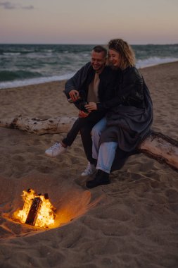Akşamları plajda ateşin yanında sıcak çay içen çift.