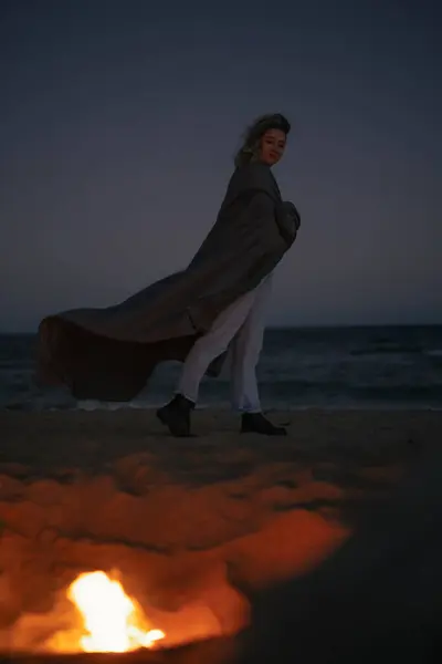 Nainen Seisoo Lähellä Nuotiota Meren Rannalla Illalla — kuvapankkivalokuva