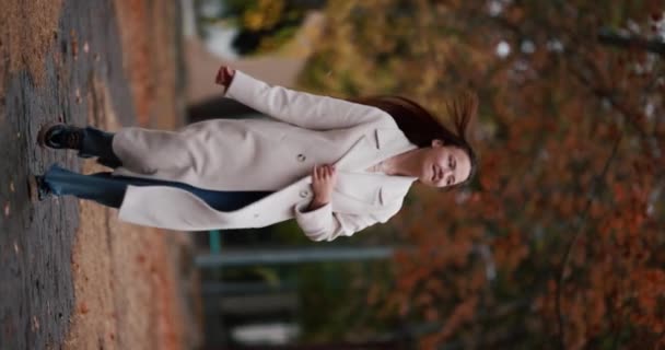 快乐的女人穿着外套跑着享受秋天的日子 慢动作的垂直录像 — 图库视频影像